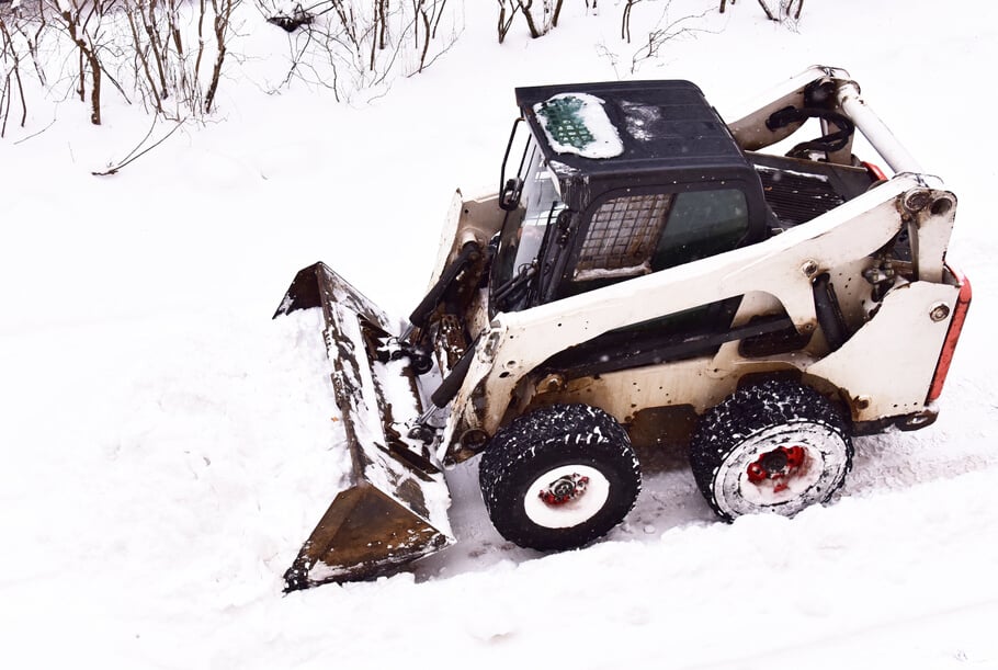 Skid-steer loader during snow removal on the road after a snowfall.